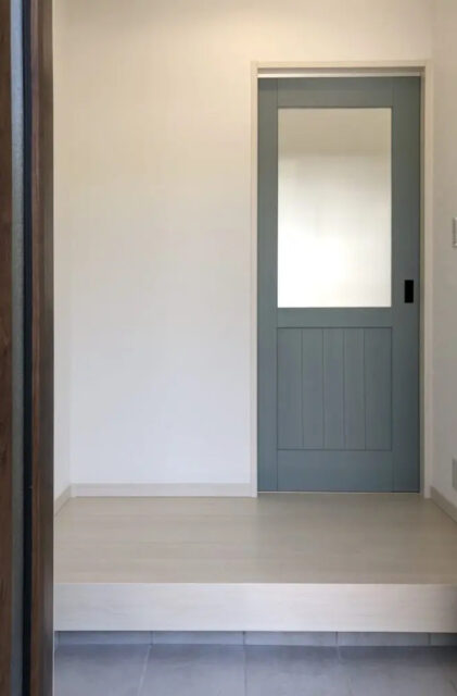 勾配天井の開放感とくすみブルーがアクセントのモノトーンで温もりを感じる平屋 - センチュリーハウス - 玄関